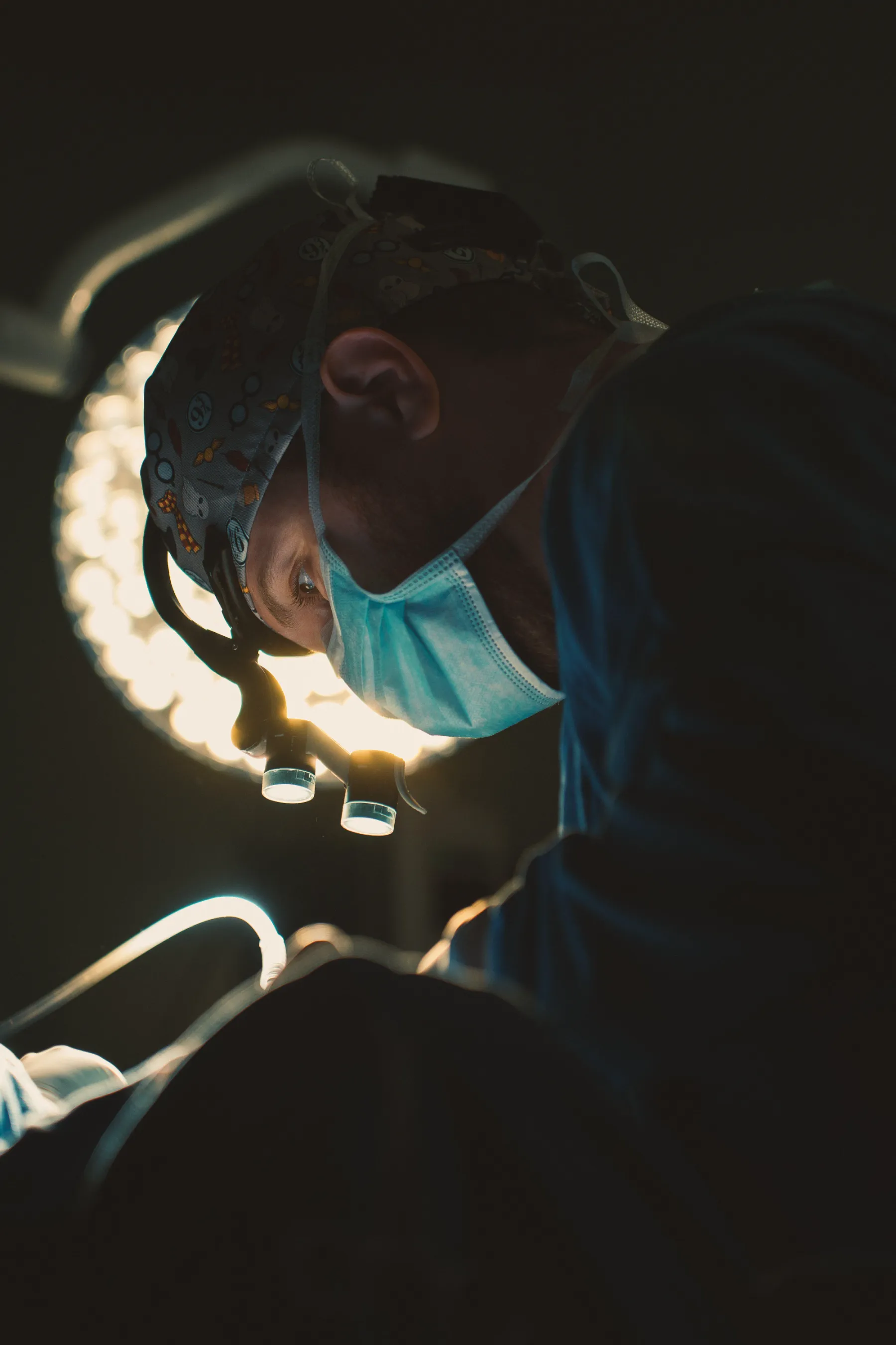 Dr. Guilherme Sachet em cirurgia, com lupa cirúrgica, sob o foco do centro cirúrgico